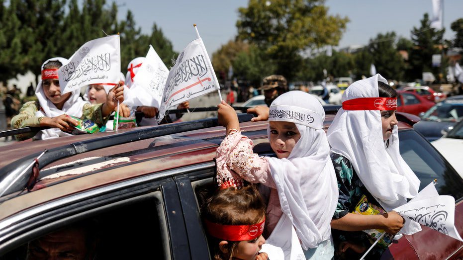 Afghanische Mädchen tragen die Flaggen des Islamischen Emirats, als sie am ersten Jahrestag des Abzugs der US-Streitkräfte aus Afghanistan teilnehmen