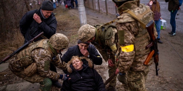 Ukrainische Soldaten kümmern sich um eine halb bewusstlose Frau, nachdem sie am Samstag, dem 5. März 2022, auf der Flucht aus der Stadt am Stadtrand von Kiew, Ukraine, den Fluss Irbin überquert haben.