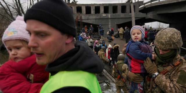 Ein ukrainischer Soldat trägt ein Kleinkind, das den Irbin-Fluss auf einer improvisierten Straße unter einer Brücke überquert, die durch einen russischen Luftangriff zerstört wurde, während er Menschen hilft, die am Samstag, dem 5. März 2022, aus der Stadt Irbin in der Ukraine fliehen. durch – Brände zur Evakuierung von Einwohnern aus zwei Städten in der Ukraine brachen am Samstag schnell zusammen, als ukrainische Beamte sagten, die Bombardierung habe die Arbeiten zur Evakuierung von Zivilisten Stunden nach der Bekanntgabe des Deals durch Russland eingestellt.