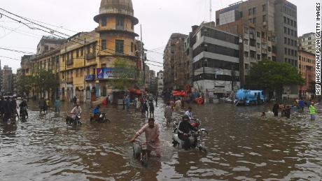 Menschen schlendern am 25. Juli nach heftigen Monsunregen in Karatschi auf einer überfluteten Straße.