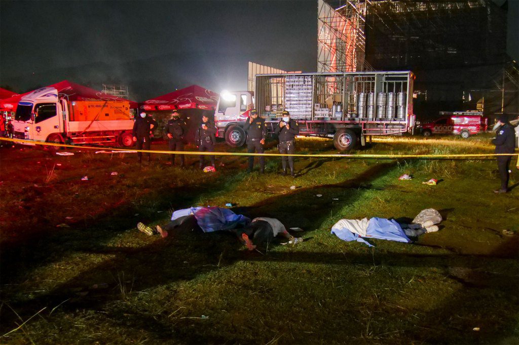 Feuerwehrleute und Polizisten stehen neben den Leichen von Menschen, die während eines Freiluftkonzerts zur Feier des Unabhängigkeitstages in Quetzaltenango, Guatemala, bei einem Ansturm ums Leben kamen.