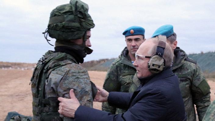Putin trägt ein schützendes Ohr und ein Auge, während er mit dem Soldaten spricht